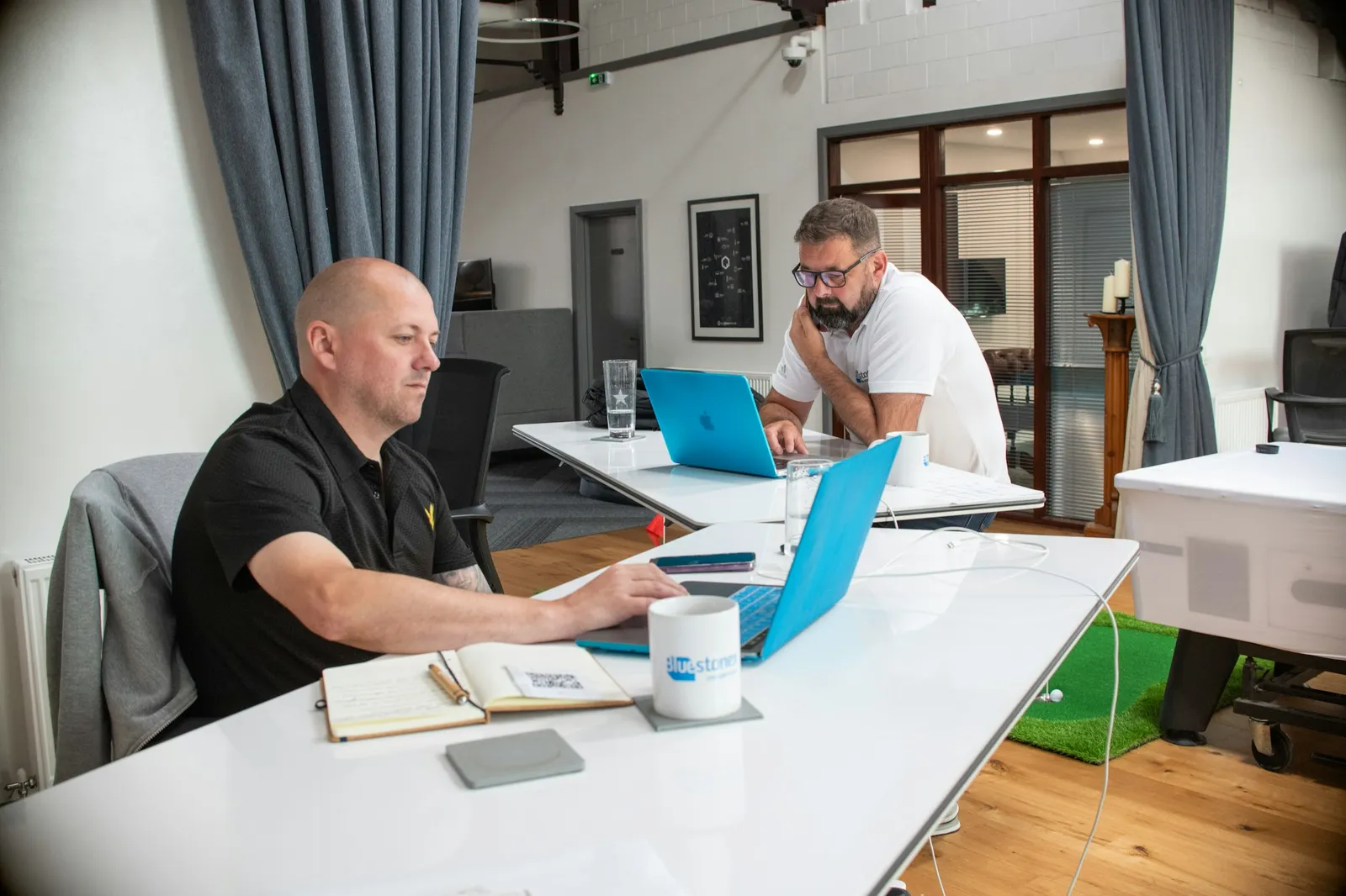 Two people working on laptops at a desk in an office